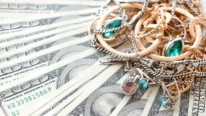 Assortment of gold and silver jewelry with gemstones on a fan of US dollar bills, representing value and investment in precious metals